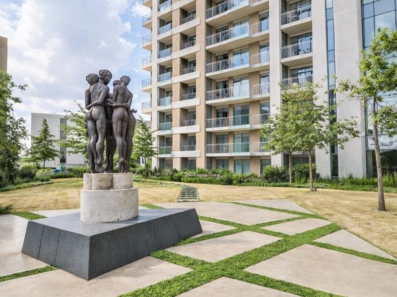 A well-maintained communal garden area featuring a central sculpture, paved pathways, and views of the modern apartment building facade with private balconies.