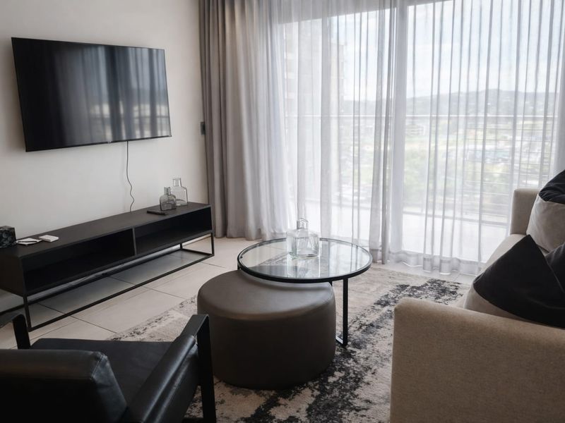 A modern living room featuring tiled flooring and large sliding glass doors with sheer curtains, providing ample natural light and access to the balcony.