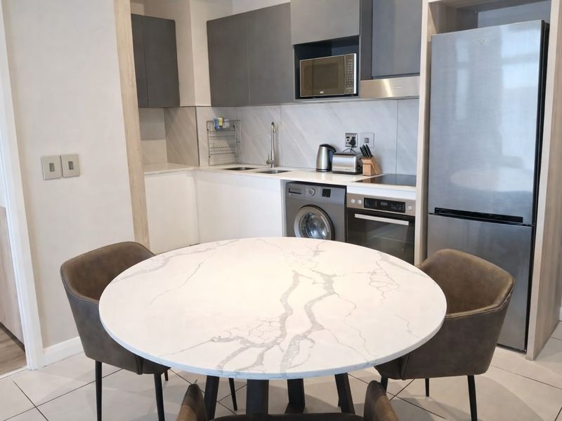 Modern open-plan kitchen featuring sleek grey and white cabinetry, integrated appliances, and high-quality stone countertops, seamlessly flowing into the dining area.
