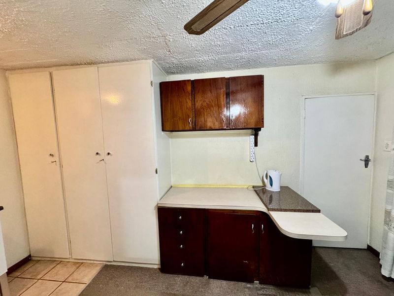 A dated kitchen area featuring built-in wooden cabinetry, laminate countertops, and a ceiling fan, requiring cosmetic updates to modernize the space.