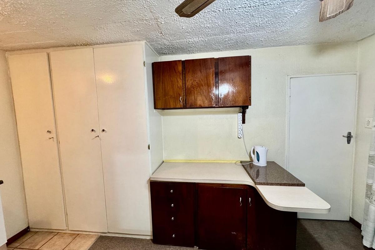 A dated kitchen area featuring built-in wooden cabinetry, laminate countertops, and a ceiling fan, requiring cosmetic updates to modernize the space.