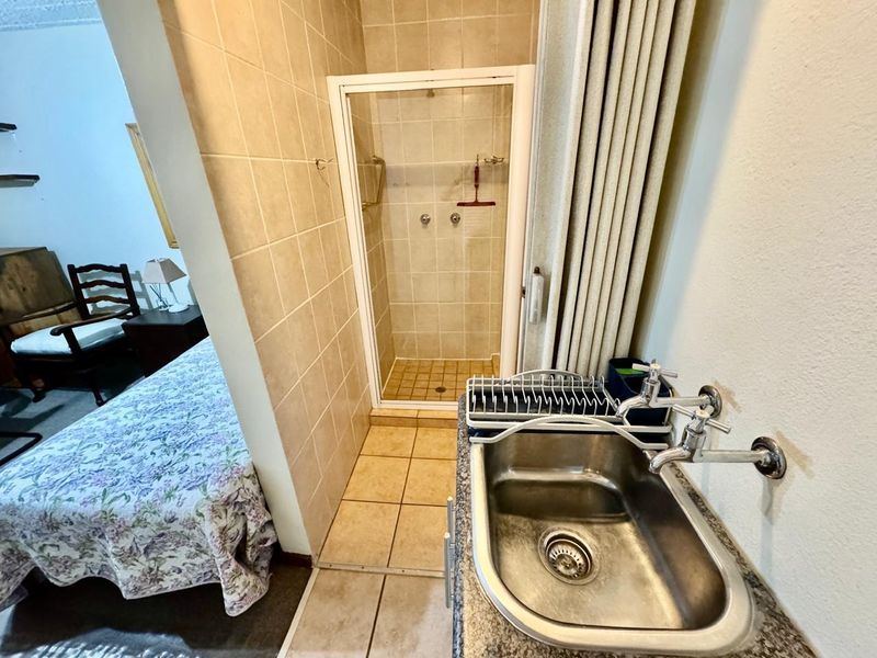 A compact bathroom area featuring a tiled shower enclosure and a functional stainless steel sink with wall-mounted taps.