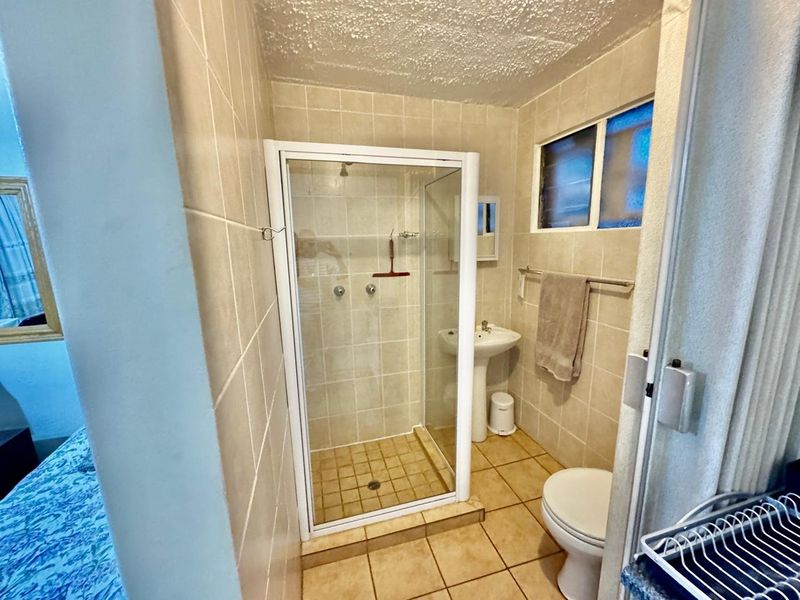 A functional bathroom featuring a shower enclosure, pedestal basin, and toilet with neutral wall and floor tiling.