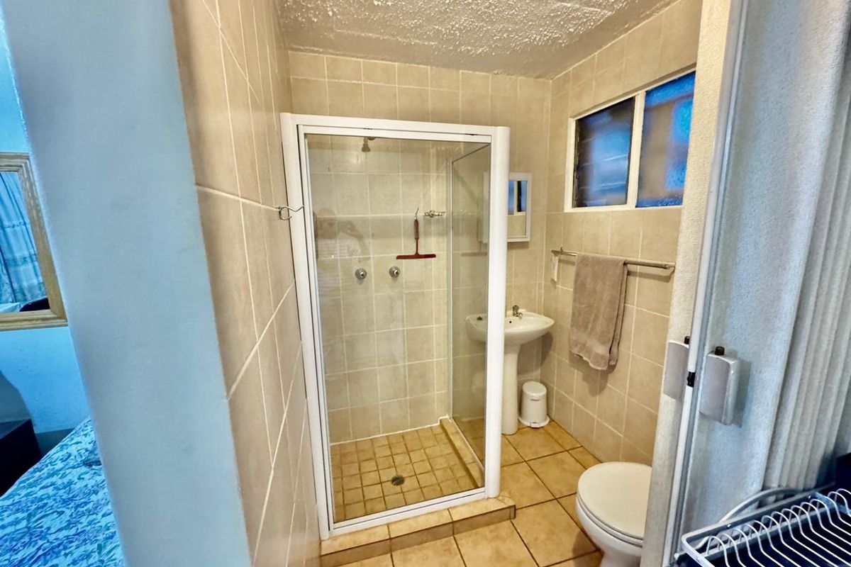 A functional bathroom featuring a shower enclosure, pedestal basin, and toilet with neutral wall and floor tiling.