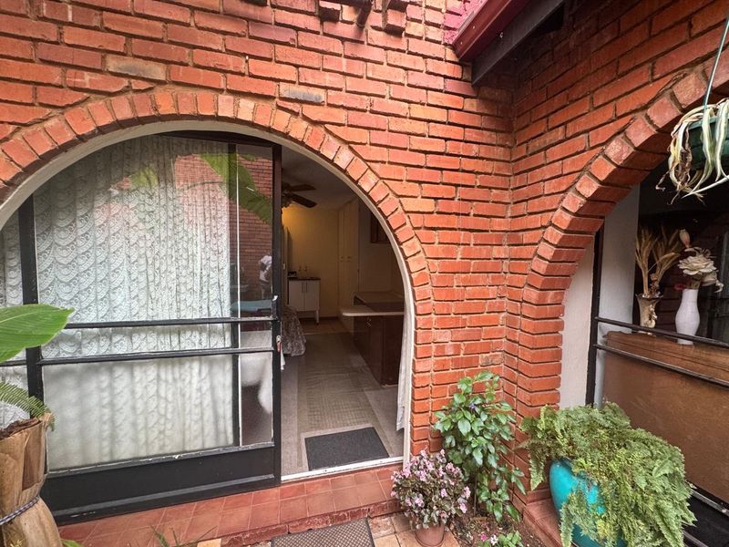 A covered patio area featuring distinctive brick archways and a sliding glass door providing access to the interior living space.