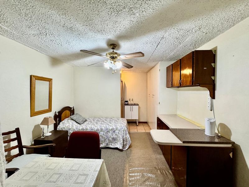 Open-plan studio apartment featuring a kitchenette with built-in cabinetry, a ceiling fan, and carpeted flooring throughout.