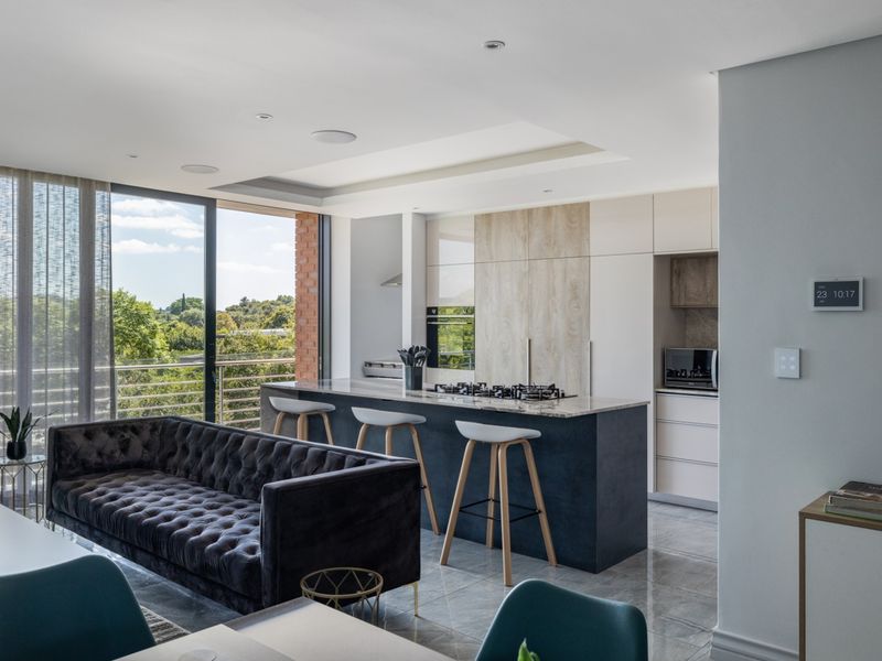 Modern open-plan living area featuring a sleek kitchen with a central island, high-end built-in appliances, and large sliding doors opening to a balcony.
