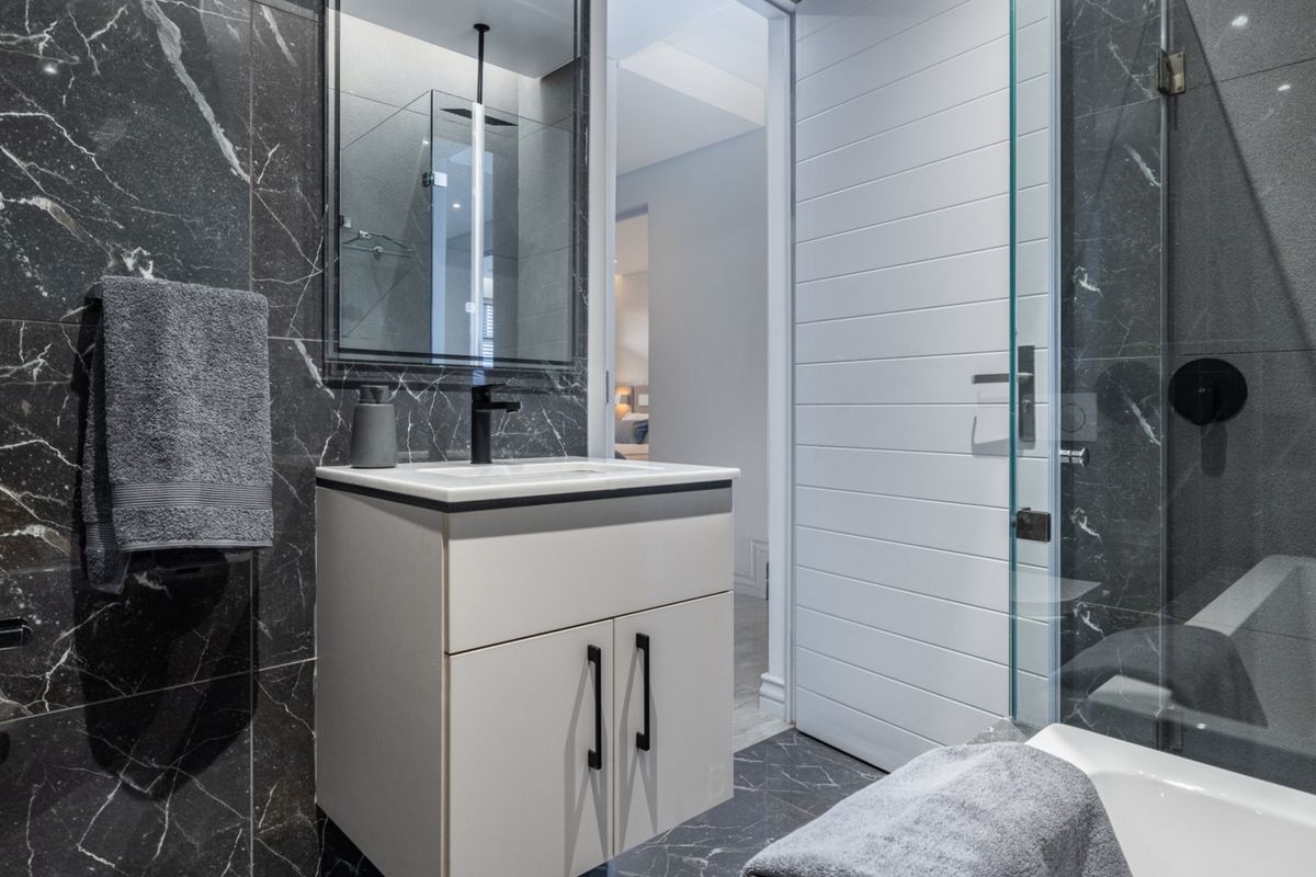 Modern bathroom featuring dark marble-look wall and floor tiles, a sleek vanity with a black mixer tap, and a glass-enclosed shower area.