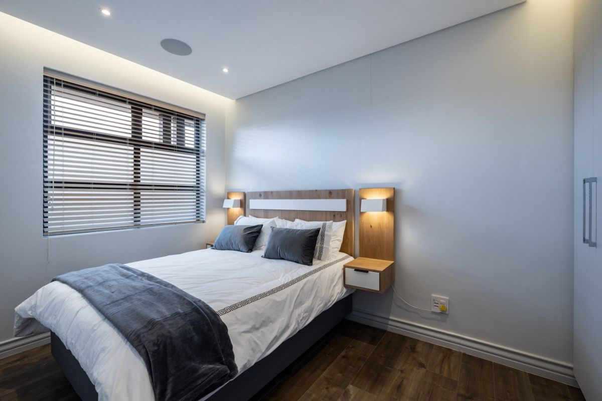 Modern bedroom featuring laminate flooring, recessed ceiling lighting, and a custom built-in headboard with integrated floating bedside tables and lighting.