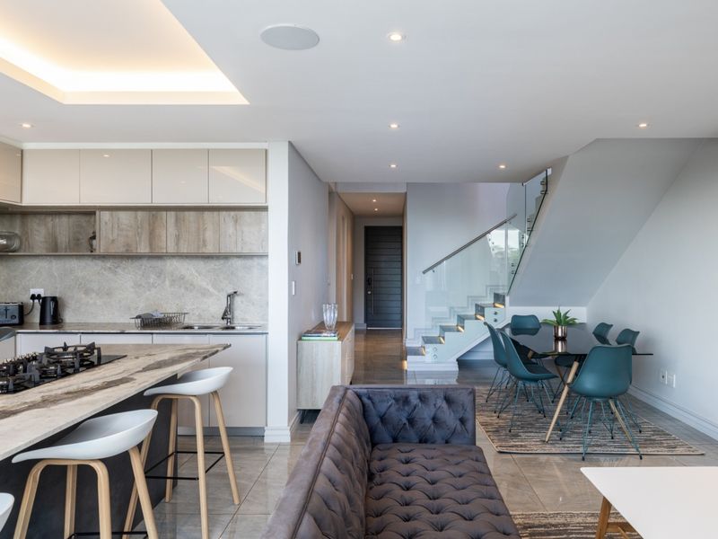 Modern open-plan living area featuring a sleek kitchen with stone island, gas hob, and a contemporary staircase with glass balustrade.