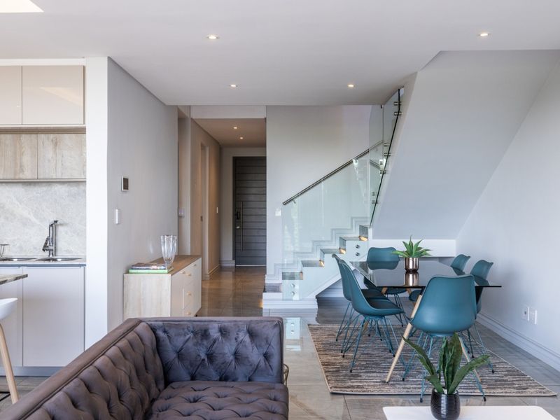 Modern open-plan living area featuring a sleek kitchen, tiled floors, recessed lighting, and a contemporary staircase with a glass balustrade.