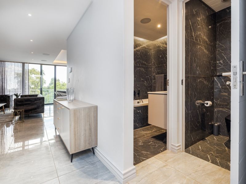 A modern hallway featuring polished marble-look flooring, leading into a contemporary bathroom with dark marble tiling and high-end fixtures.