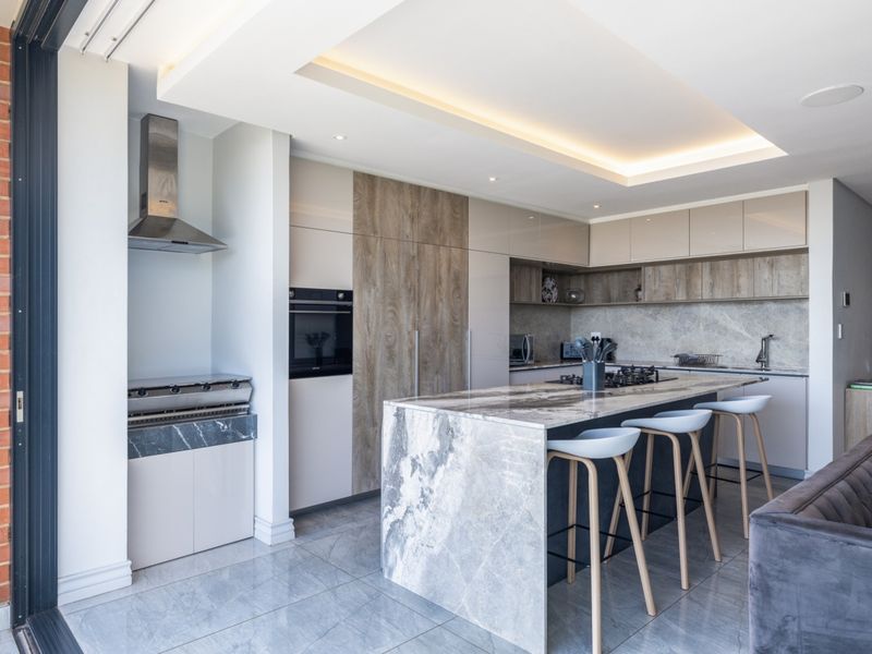 Modern open-plan kitchen featuring a large stone island, integrated appliances, sleek cabinetry, and recessed ceiling lighting, seamlessly connecting to the living area.