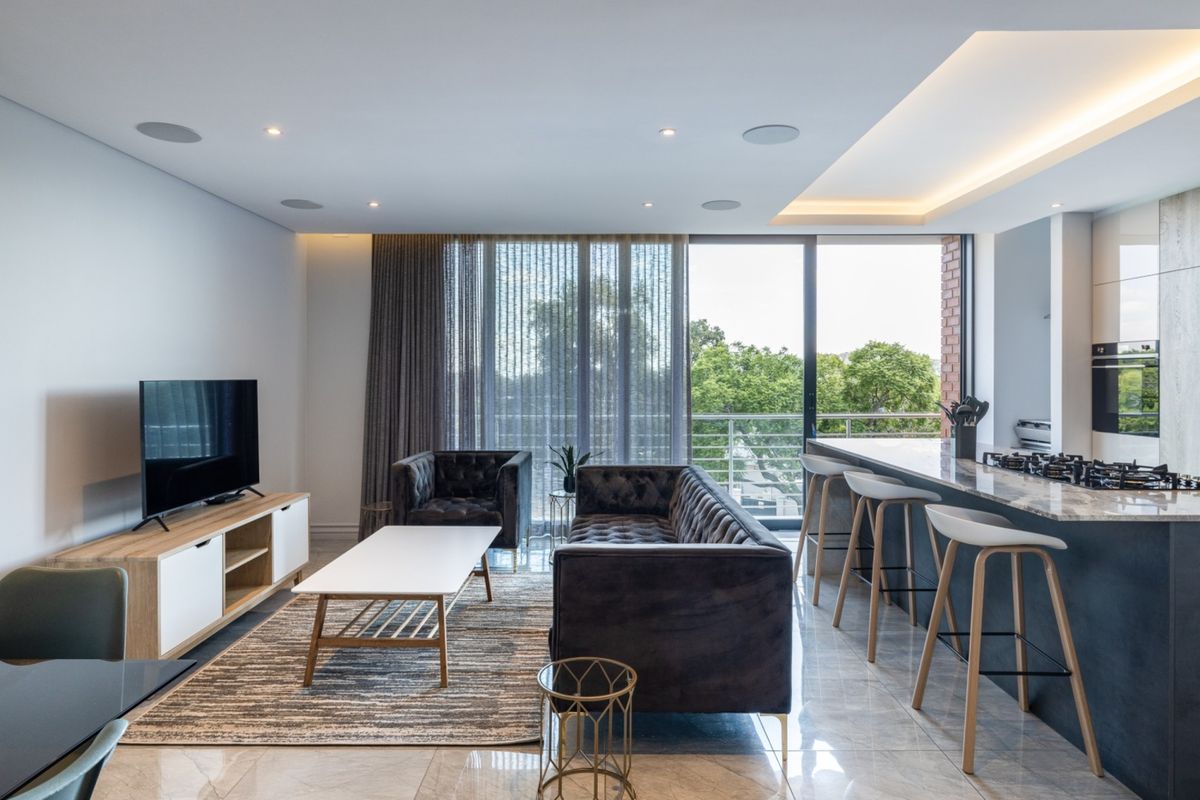 Modern open-plan living area featuring a sleek kitchen island with gas cooktop, recessed ceiling lighting, and large sliding doors leading to a balcony.