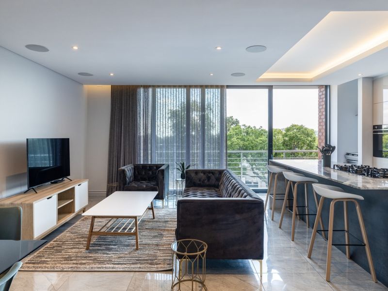 Modern open-plan living area featuring a sleek kitchen island with gas cooktop, recessed ceiling lighting, and large sliding doors leading to a balcony.