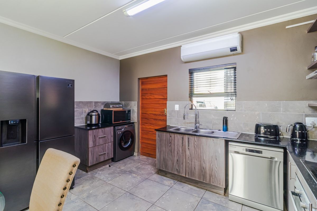 Modern kitchen featuring dark wood-grain cabinetry, stone countertops, double basin sink, tiled backsplash, and a wall-mounted air conditioning unit.