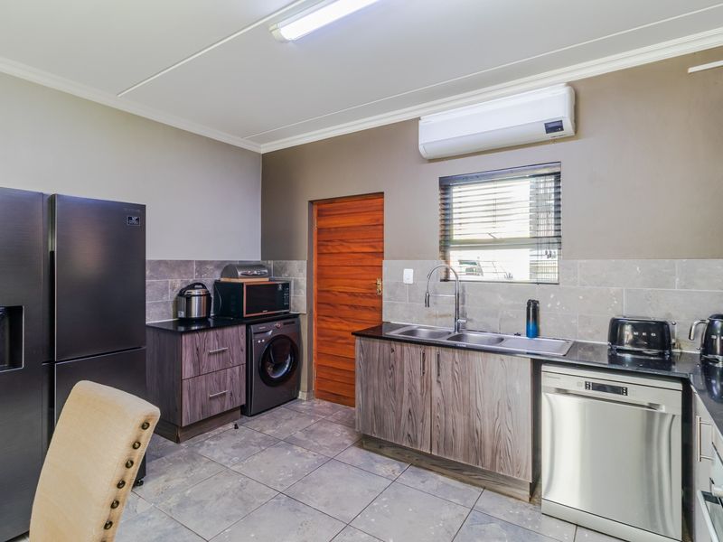 Modern kitchen featuring dark wood-grain cabinetry, stone countertops, double basin sink, tiled backsplash, and a wall-mounted air conditioning unit.
