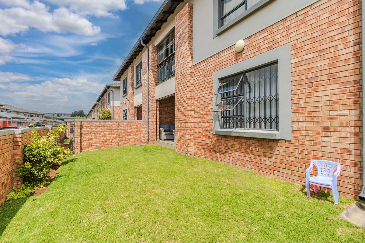A view of the rear exterior of the apartment building, featuring a private lawn area, face brick facade, and secure window fittings.