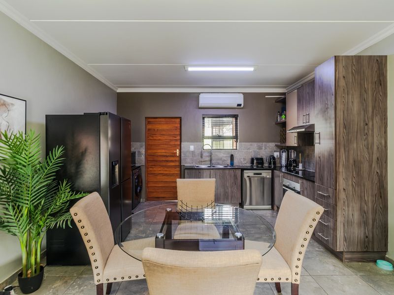 Open-plan kitchen and dining area featuring modern wood-finish cabinetry, stone countertops, integrated appliances, and tiled flooring with an installed air conditioning unit.