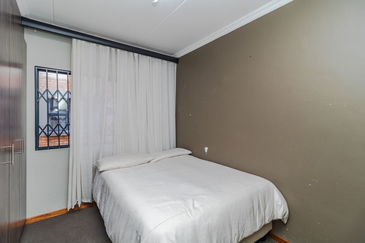 A bedroom featuring a built-in wardrobe, security gate on the window, and neutral wall finishes.