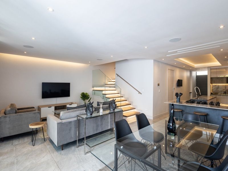 Modern open-plan living area featuring a sleek kitchen with island, dining space, and a contemporary staircase with integrated lighting and glass balustrade.