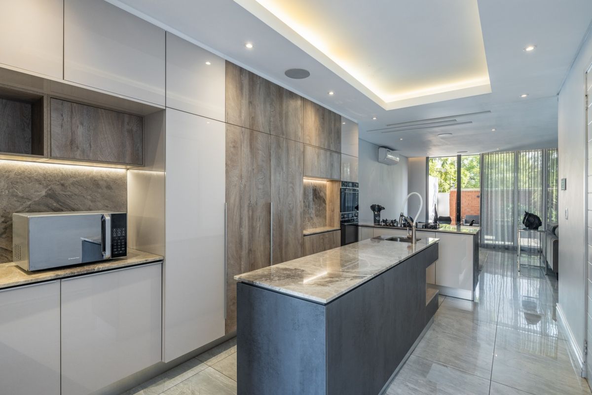 Modern kitchen featuring high-gloss and wood-grain cabinetry, a stone-topped island, integrated appliances, and elegant recessed lighting with polished tiled floors.