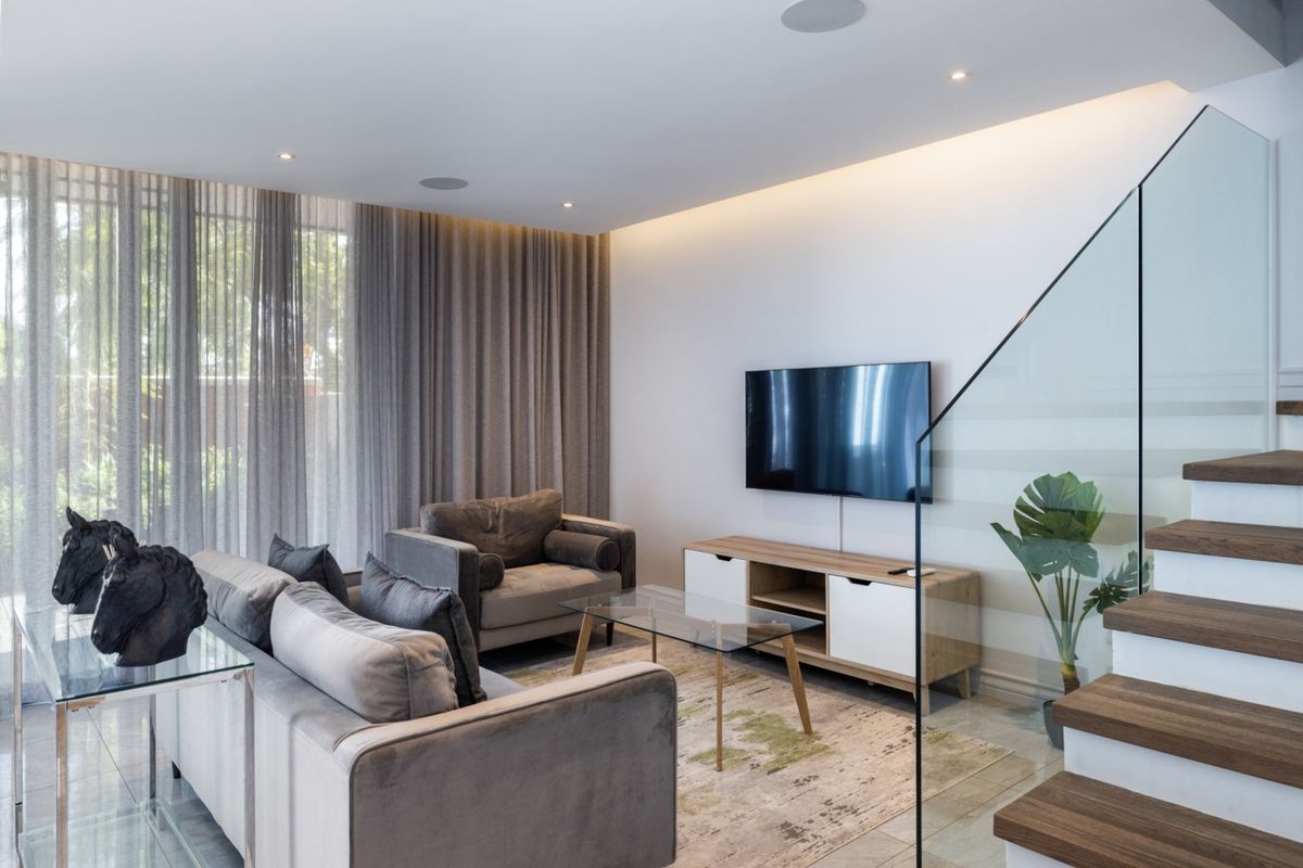 Modern living room featuring tiled flooring, a glass balustrade staircase, recessed ceiling lighting, and floor-to-ceiling curtains.