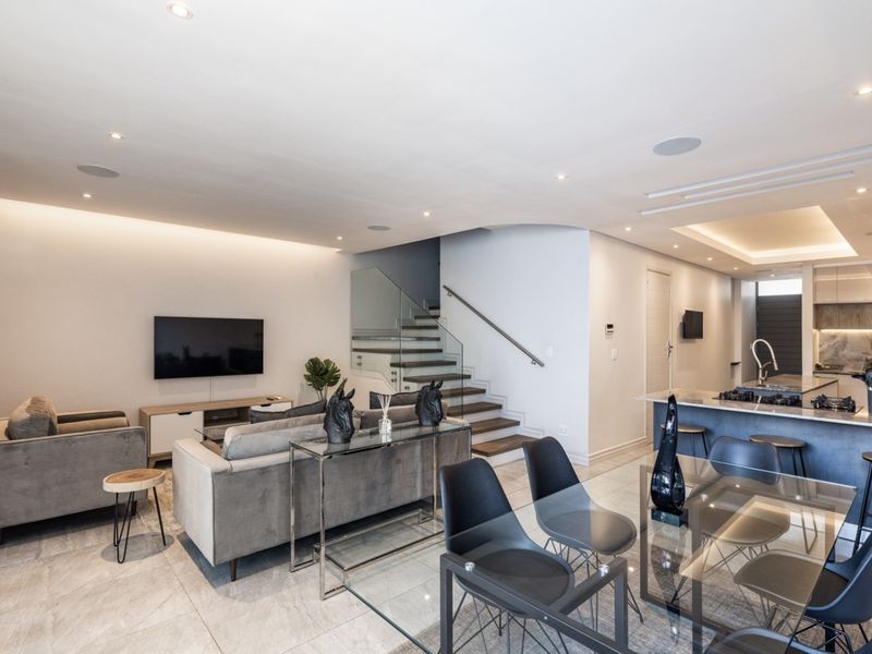 Modern open-plan living area featuring a sleek kitchen with island, dining space, and a contemporary staircase with glass balustrade and recessed lighting.