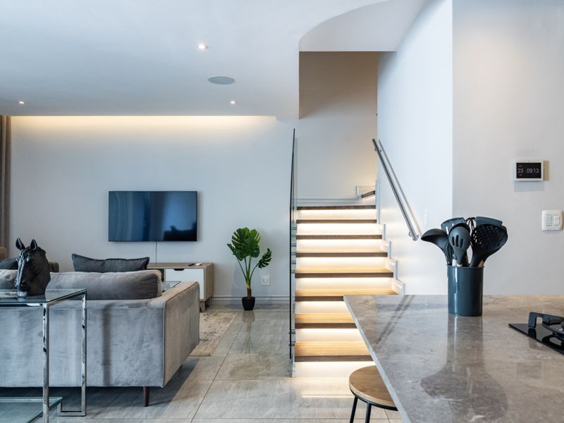 Modern open-plan living area featuring a sleek staircase with integrated lighting, stone kitchen countertops, and high-quality tiled flooring throughout.