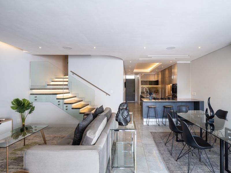 Modern open-plan living area featuring a sleek kitchen with island, contemporary staircase with glass balustrade, and high-quality finishes throughout.