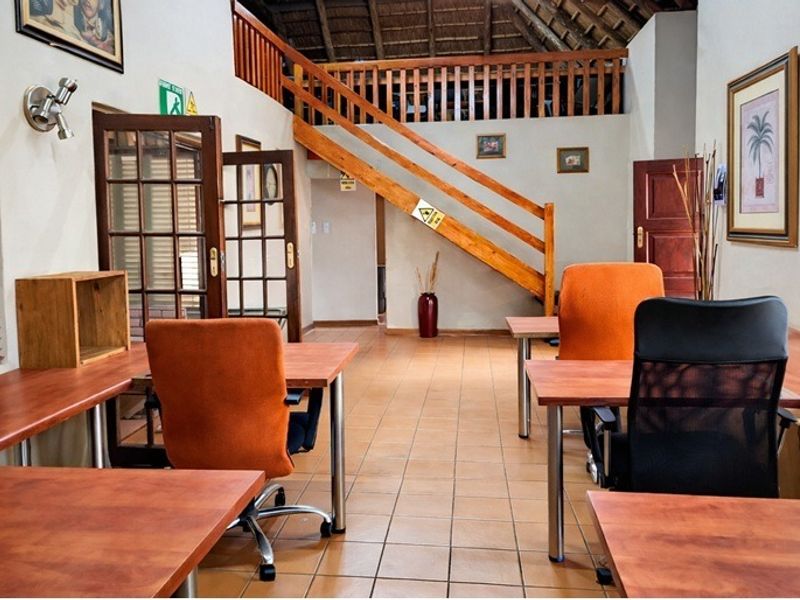 Spacious office area featuring tiled flooring, a timber staircase with balustrade, and a high thatched ceiling, providing a unique and functional workspace.