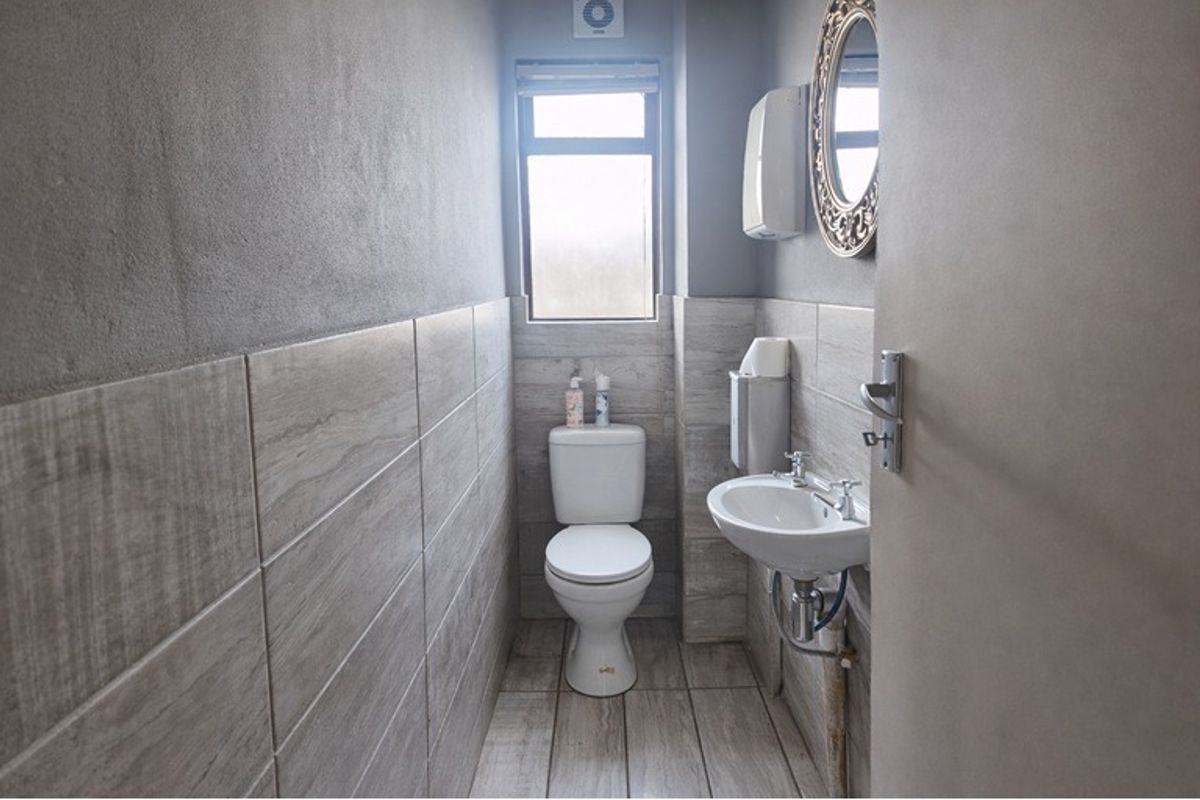 A compact, modern bathroom featuring neutral wood-look floor and wall tiles, a pedestal basin, and a standard toilet.