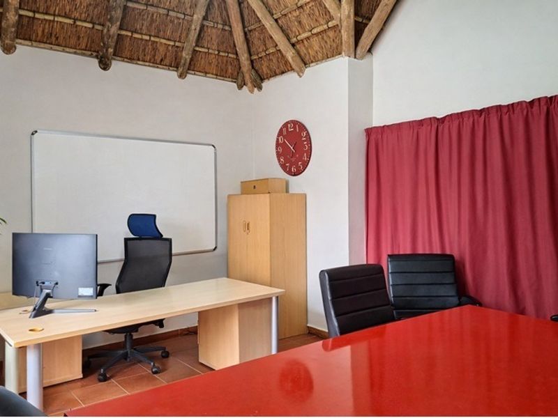 A functional home office space featuring a high thatched ceiling with exposed timber rafters and tiled flooring, suitable for a professional work environment.