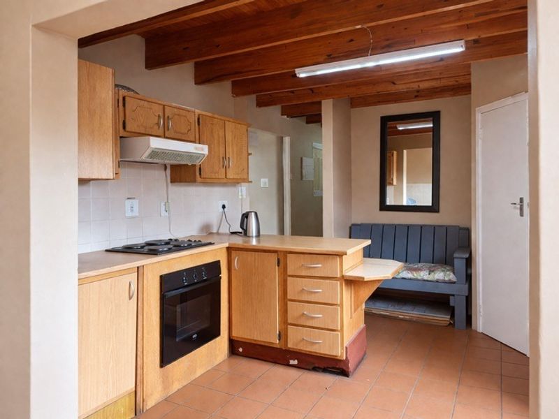 A functional kitchen featuring wooden cabinetry, built-in oven, hob, extractor fan, and exposed timber ceiling beams with tiled flooring.