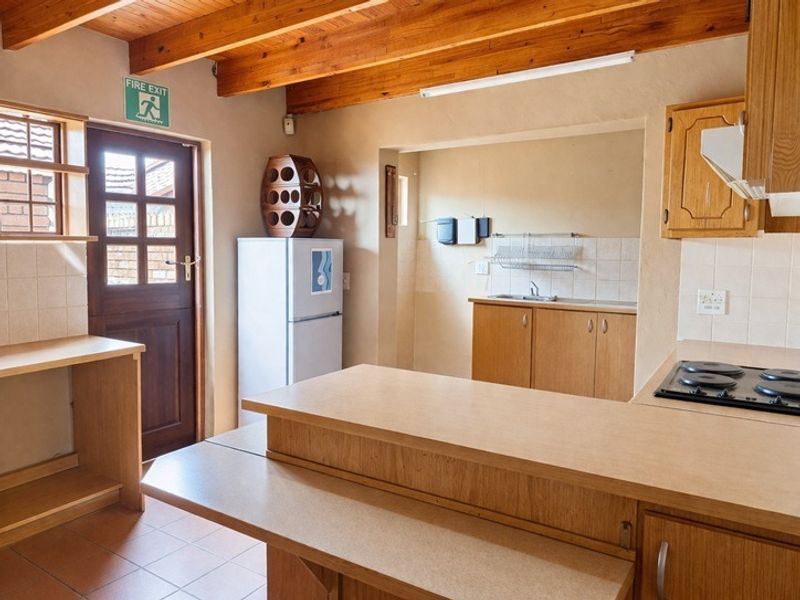 A functional kitchen featuring exposed timber ceiling beams, laminate cabinetry, and a breakfast bar, with a separate scullery area and direct exterior access.