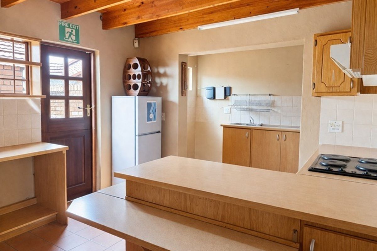 A functional kitchen featuring exposed timber ceiling beams, laminate cabinetry, and a breakfast bar, with a separate scullery area and direct exterior access.
