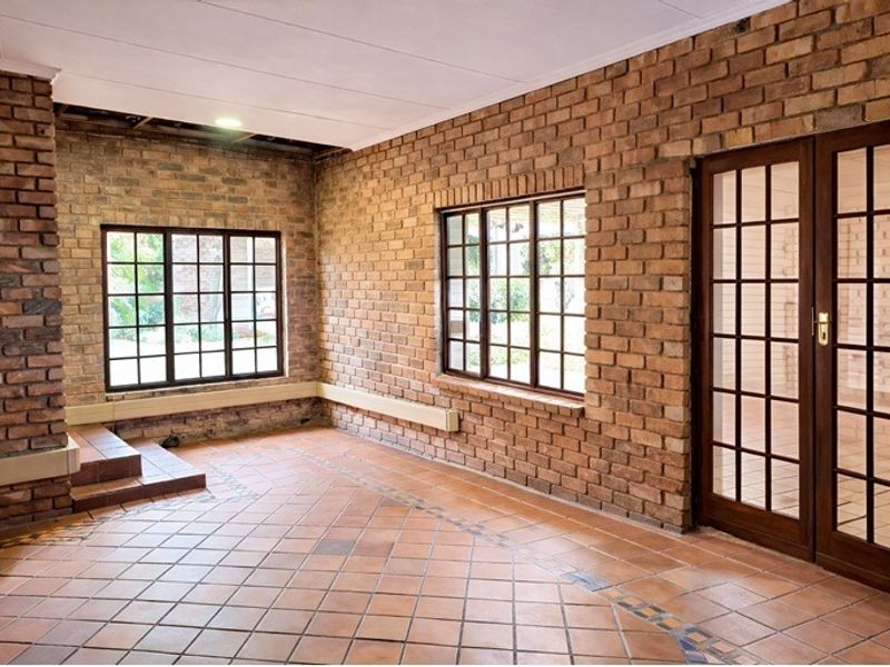 Spacious living area featuring exposed brick walls, terracotta tile flooring, and classic french doors. Requires ceiling repairs to complete the space.