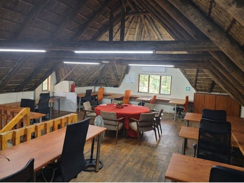 Spacious attic-style office area featuring exposed timber rafters, a traditional thatched roof, and timber flooring, providing a unique and functional workspace.