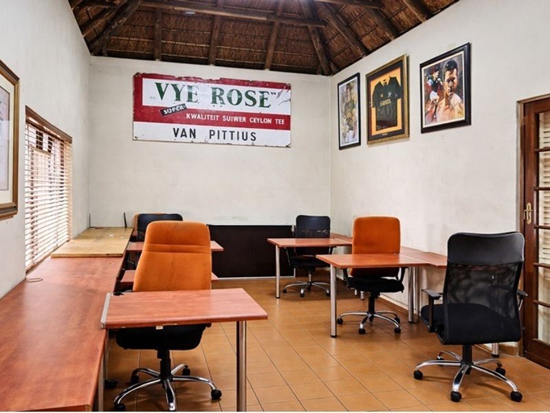 A functional office space featuring a traditional thatched roof with exposed timber rafters, tiled flooring, and a classic wooden french door.