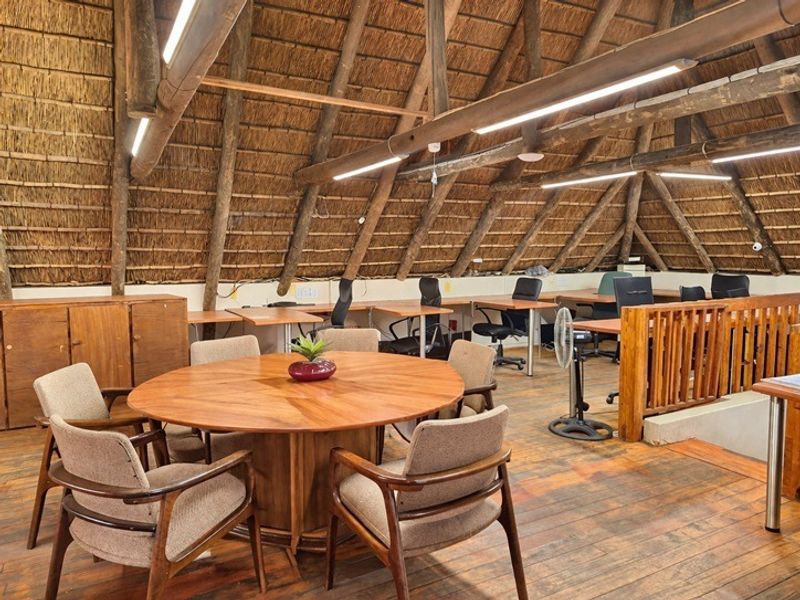 Spacious attic-style office featuring exposed timber rafters, a traditional thatched roof, and warm timber flooring with a functional open-plan layout.