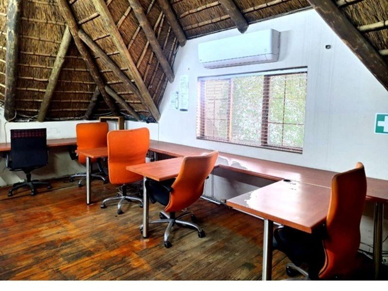 Office space featuring a unique thatched roof with exposed timber rafters, timber flooring, and a built-in desk setup with air conditioning.