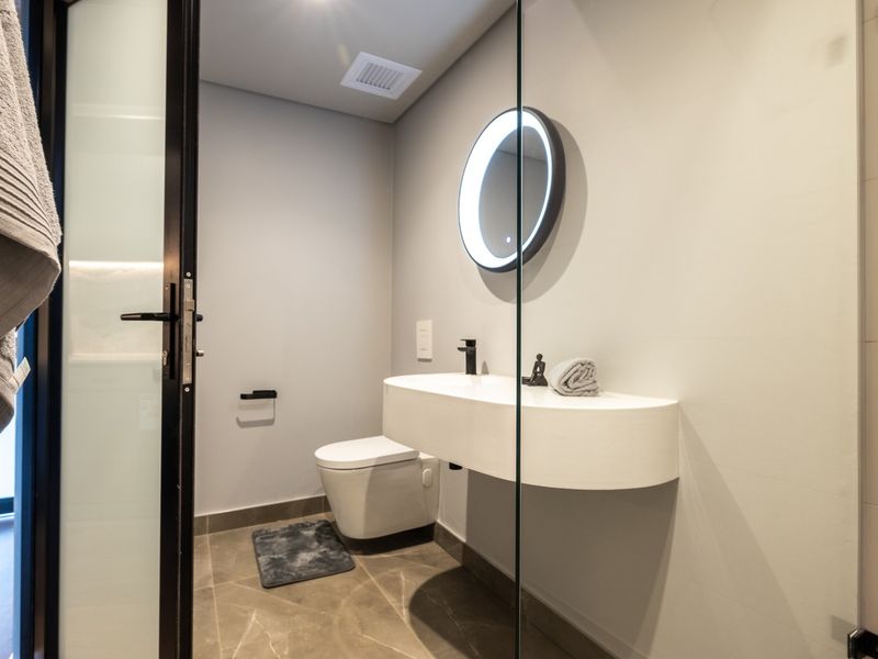 Modern bathroom featuring a sleek wall-mounted vanity, back-to-wall toilet, backlit circular mirror, and a glass shower screen with contemporary black fixtures.