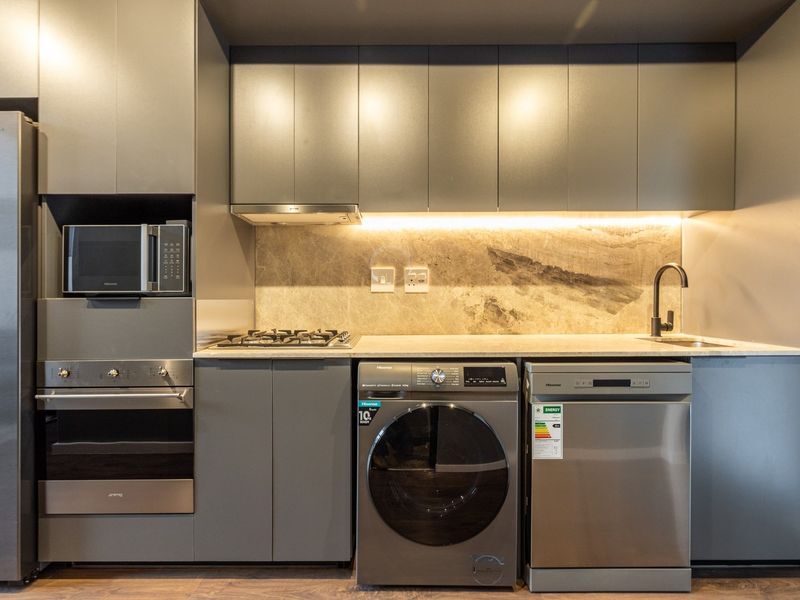 Modern kitchen featuring sleek grey cabinetry, stone backsplash, integrated appliances, gas hob, and high-quality finishes throughout.