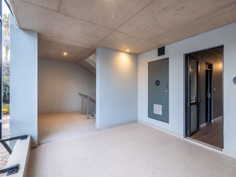 A modern, clean apartment entrance area featuring concrete ceilings, tiled floors, and access to a staircase, presenting a well-maintained and contemporary aesthetic.