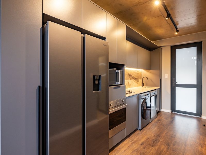 Modern galley kitchen featuring sleek grey cabinetry, stone countertops, integrated appliances, and an industrial-style exposed concrete ceiling with track lighting.