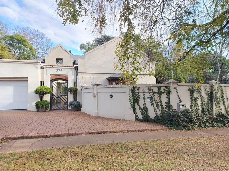 Front elevation of a cottage featuring a brick paved driveway, secure gated entrance, integrated garage, and perimeter wall with electric fencing.
