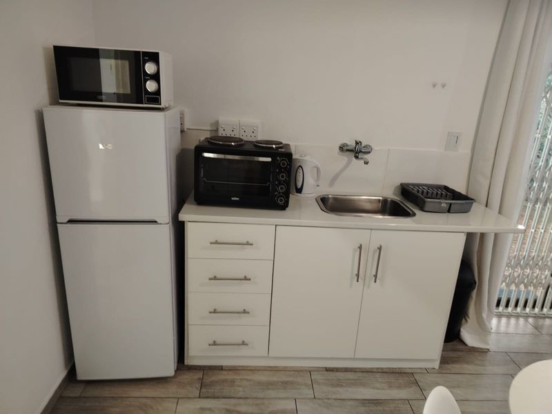 A compact kitchenette featuring white cabinetry, a stainless steel sink, and tiled flooring, providing essential prep space in a cottage setting.