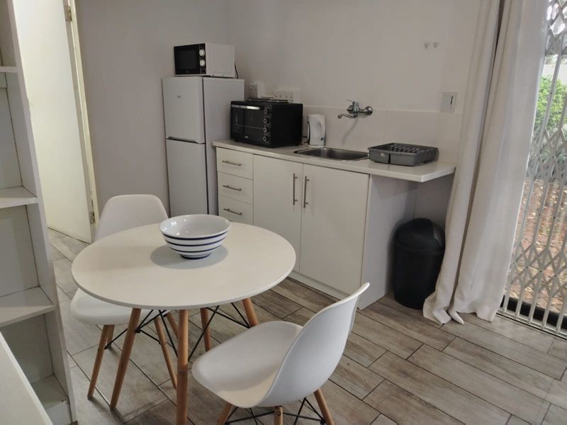 Compact kitchen area featuring white cabinetry, stainless steel sink, and tiled flooring, with direct access to an outdoor space via a sliding door.