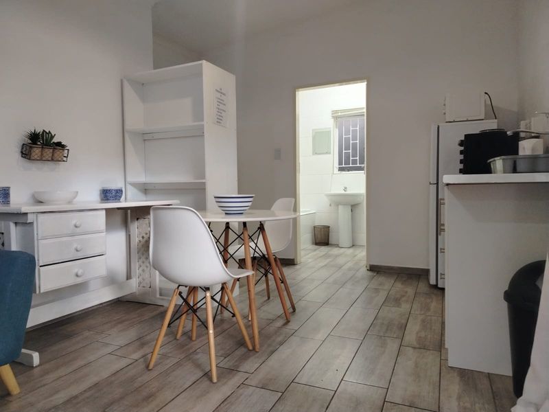 Open plan living area with wood-look tiled flooring, featuring built-in shelving and a view through to the adjacent bathroom with pedestal basin.