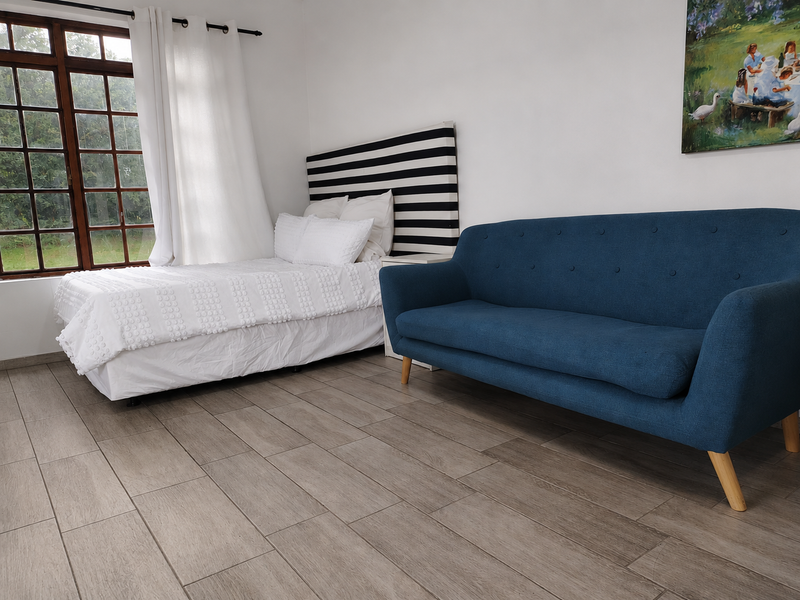 A bright bedroom featuring wood-look floor tiles and a large timber-framed window providing natural light.